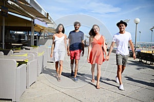 Groupe of young people man and woman walking on seaside of touristic resort during sunny summer day