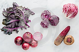 Groups of red and purple vegetables on a marble surface.