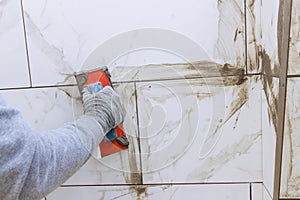 Grouting ceramic tiles with tilers filling space between tiles using a rubber trowel.