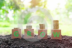 Grow, save and invest money concept. Wooden blocks with increasing stack of coins on natural background.