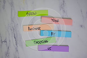 Grow Your Business By Chossing Us write on sticky notes isolated on Wooden Table