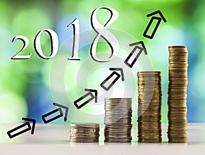 Growing coins stacks with green and blue sparkling bokeh background and 2018 chart arrows