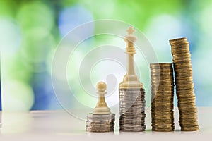 Growing coins stacks with green and blue sparkling bokeh background. Chess figures standing on coins meaning power and career