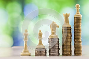 Growing coins stacks with green and blue sparkling bokeh background. Chess figures standing on coins meaning power and career