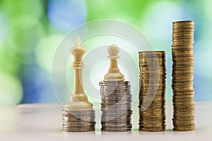 Growing coins stacks with green and blue sparkling bokeh background. Chess figures standing on coins meaning power and career