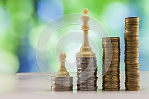 Growing coins stacks with green and blue sparkling bokeh background. Chess figures standing on coins meaning power and career