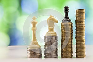 Growing coins stacks with green and blue sparkling bokeh background. Chess figures standing on coins meaning power and career