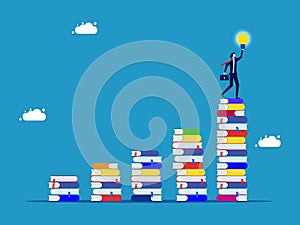 Growing knowledge or learning hierarchy. Businessman holding a light bulb on a growing pile of books