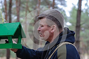 A grown man puts food in a Green wooden feeder for wild birds an