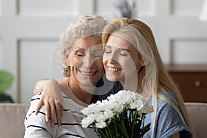 Grownup daughter greeting senior mother presenting flowers