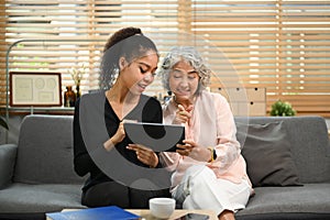 Grownup daughter teaching interested elderly mother how to use a tablet or shows some application. Elderly, technology