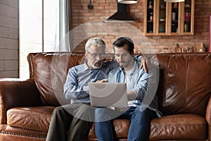 Grownup son and old father use laptop at home