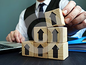 Growth business concept. Businessman makes ladder of success from blocks with arrows