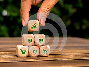 Growth graph icon block in hand put on top of wood pyramid cube blocks with green shopping cart symbol on desk and leaf background