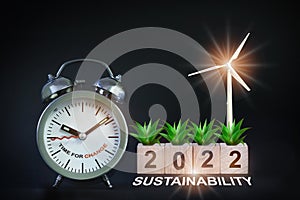 Growth plant and turbine on wooden cube new year 2022 with alarm clock on black background