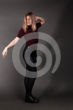 Growth Portrait of the blonde in the red sweater with short sleeves, leather trousers and boots. Studio shot on dark gray