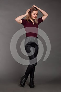 Growth Portrait of the blonde in the red sweater with short sleeves, leather trousers and boots. Studio shot on dark gray