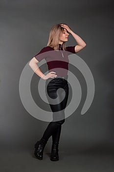 Growth Portrait of the blonde in the red sweater with short sleeves, leather trousers and boots. Studio shot on dark gray