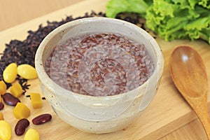 Gruel in white ceramic bowl with red bean, ginkgo and lettuce and wooden spoon on wooden cutting board