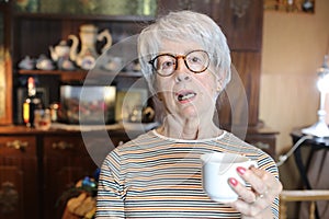 Grumpy looking senior woman holding coffee cup