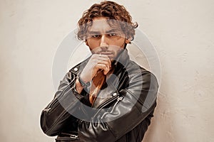 Young and and thoughtful male model with curly hair posing in a studio wearing leather jacket