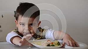 Grumpy two years old boy playing with food and refusing to eat