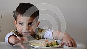 Grumpy two years old boy playing with food and refusing to eat