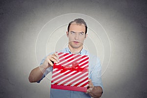 Grumpy unhappy upset man holding red gift box very displeased