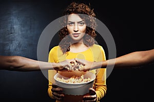 Grumpy woman holding popcorn bucket and doesn`t want to share