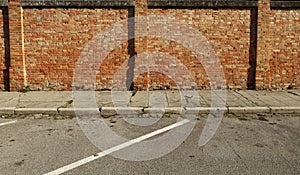 Grunge brick wall made of red and yellow bricks, a weathered sidewalk and an asphalt street.