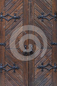 Grunge brown wooden door with forged hinges close up.