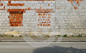 Grunge concrete block wall with bricks walled windows. Concrete sidewalk and street in front