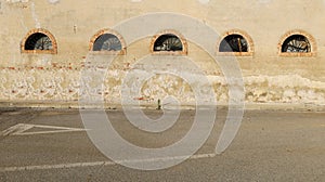 Grunge peeled plaster wall with old semicircular windows. Concrete sidewalk and street in front