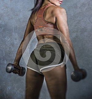 Grunge sport advertising style portrait of young athletic woman with strong back and fit body holding dumbbells in fitness trainin