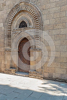 Grunge wooden ornate aged vaulted arched door on exterior decorated stone bricks wall