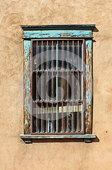 Grungy barred window on stucco wall with peeling turquoise paint