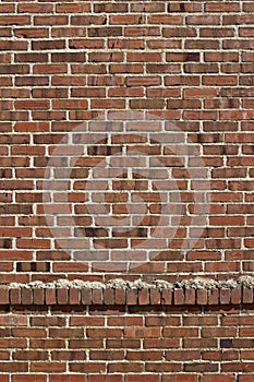 Grungy old exterior red and brown brick wall texture background with a header row of protruding bricks