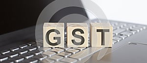 GST abbreviation stands for written on a wooden cube on laptop