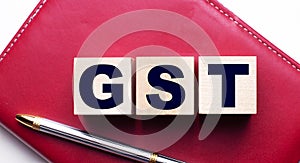 GST Goods and services tax made up of wooden cubes that stand on a burgundy notebook near the pen. Business concept