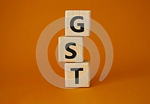 GST - Goods and Services Tax symbol. Concept word GST on wooden cubes. Beautiful orange background. Business and GST concept. Copy