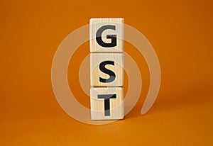 GST - Goods and Services Tax symbol. Concept word GST on wooden cubes. Beautiful orange background. Business and GST concept. Copy