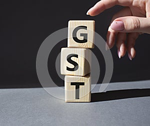 GST - Goods and Services Tax symbol. Concept word GST on wooden cubes. Businessman hand. Beautiful grey background. Business and