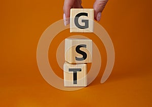 GST - Goods and Services Tax symbol. Concept word GST on wooden cubes. Businessman hand. Beautiful orange background. Business and