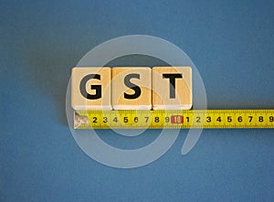 GST, goods and services tax symbol. The word GST, goods and services tax on cubes arranged behind the ruler on beautiful blue