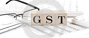 GST - Goods and Services Tax written on wooden cube with keyboard , calculator, chart,glasses.Business concept