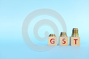 GST letters on wooden blocks in blue background increasing stack of coins. Increase on goods and services tax