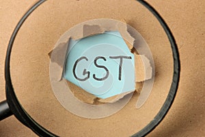 GST word and torn paper and magnifier. Taxes on the background of craft paper. top view