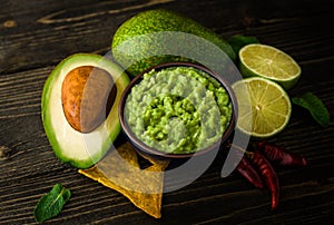 Guacamole in blue bowl with tortilla chips and lemon on natural wooden desk.