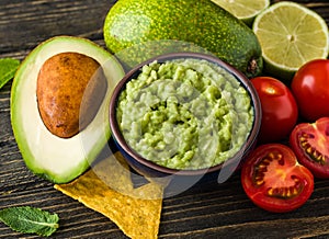 Guacamole in blue bowl with tortilla chips and lemon on natural wooden desk.