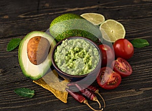 Guacamole in blue bowl with tortilla chips and lemon on natural wooden desk.